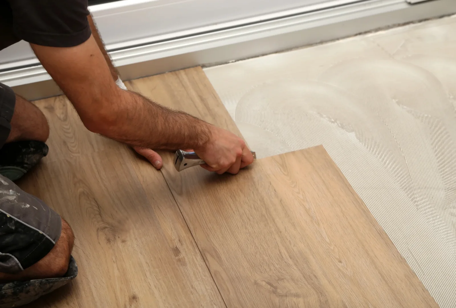 Installer fitting a luxury vinyl plank into place with a utility knife